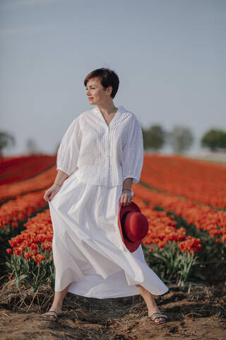 Porträt einer modischen, weiß gekleideten Frau vor einem Tulpenfeld, lizenzfreies Stockfoto