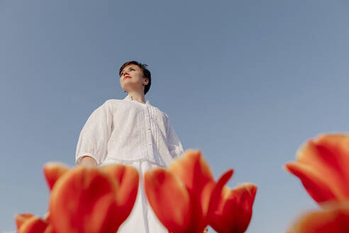 Porträt einer weiß gekleideten Frau in einem Tulpenfeld vor blauem Himmel - OGF00360