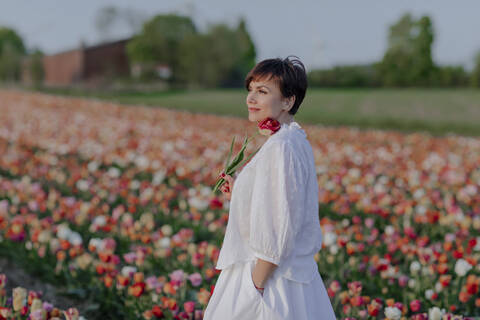 Portrait of smiling woman dressed in white standing in tulip field stock photo