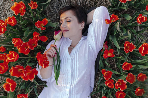 Porträt einer lächelnden Frau mit geschlossenen Augen zwischen Tulpen liegend - OGF00365