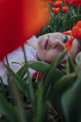 Portrait of woman lying between tulips - OGF00367