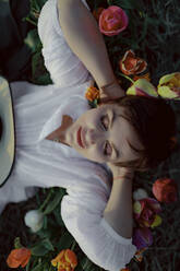 Porträt einer Frau mit geschlossenen Augen, die zwischen Tulpen auf dem Boden liegt - OGF00371