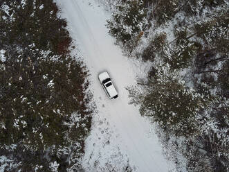 Spain, Asturias, Cornellana, Aerial view of 4x4 car driving along snow-covered forest road - VEGF02110