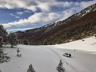 Spain, Asturias, Cornellana, 4x4 car driving across snow-covered mountain valley - VEGF02111
