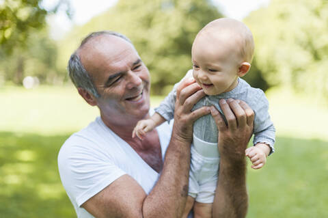 Smiling senior man holding baby girl in a park stock photo