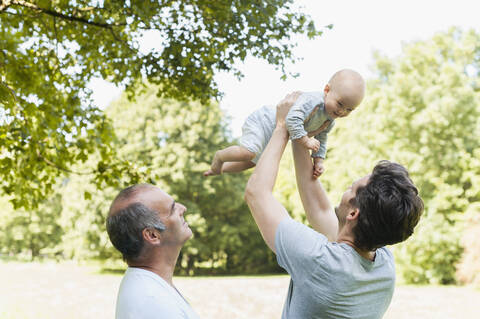 Senior man spending time with his adult son and his granddaughter in a park stock photo