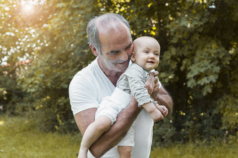 Smiling senior man holding baby girl on his arm in a park stock photo