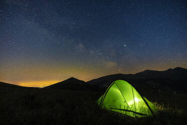 Italy, Green illuminated tent pitched in Piani di Ragnolo plateau at night - LOMF01058