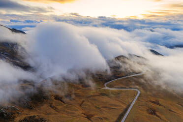 Luftaufnahme einer Drohne von Nebel über einer Panoramastraße, die den Giau-Pass in einem Wolkenmeer bei Sonnenuntergang überquert, Dolomiten, Provinz Belluno, Venetien, Italien, Europa - RHPLF14799