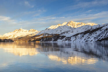 Von der Sonne beleuchtete Berge bei Sonnenuntergang, die sich auf der eisigen Oberfläche des Silsersees spiegeln, Engadin, Graubünden, Schweiz, Europa - RHPLF14839