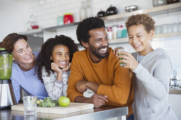 Multiethnische Familie macht und trinkt gesunden grünen Smoothie in der Küche - CAIF26962