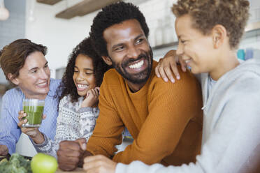 Lächelnde multiethnische Familie trinkt gesunden grünen Smoothie in der Küche - CAIF26964