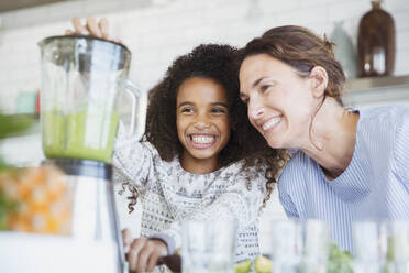 Lächelnde, begeisterte Mutter und Tochter bei der Zubereitung eines gesunden grünen Smoothies im Mixer in der Küche - CAIF26972