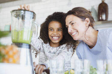 Smiling, enthusiastic mother and daughter making healthy green smoothie in blender in kitchen - CAIF26972