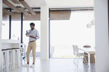 Businessman drinking coffee and using digital tablet in kitchen - CAIF26979