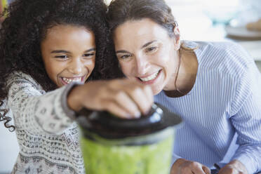 Mother and daughter making healthy green smoothie in blender - CAIF26986