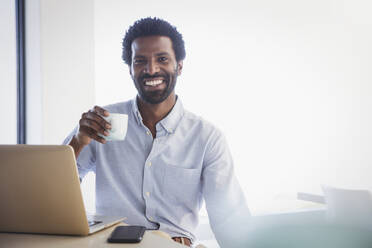 Porträt lächelnder, selbstbewusster Geschäftsmann, der am Laptop Kaffee trinkt - CAIF27003