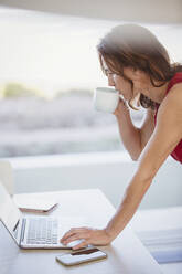 Geschäftsfrau trinkt Kaffee und arbeitet am Laptop - CAIF27004