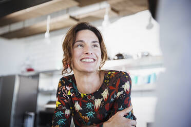 Smiling brunette woman listening, looking away in kitchen - CAIF27013