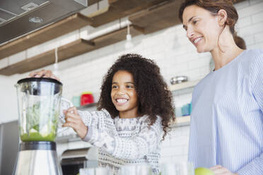 Mother and daughter making healthy green smoothie in blender in kitchen - CAIF27032