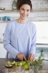 Porträt lächelnde Frau schneiden gesunde Äpfel und Avocado in der Küche - CAIF27041