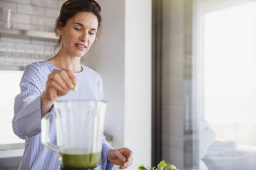 Frau macht gesunden grünen Smoothie im Mixer in der Küche - CAIF27044