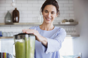 Lächelnde Frau macht gesunden grünen Smoothie in der Küche - CAIF27046