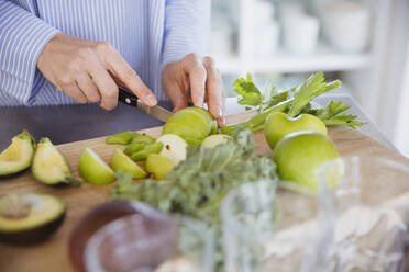 Frau schneidet gesunde grüne Äpfel und Gemüse auf einem Schneidebrett - CAIF27049