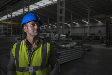 Portrait confident male worker looking away in dark factory - CAIF27058