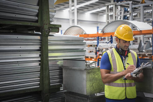 Männlicher Arbeiter mit Klemmbrett bei der Arbeit in einer Stahlfabrik - CAIF27060