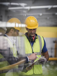 Männlicher Vorgesetzter und Arbeiter mit Klemmbrett im Gespräch in einer Fabrik - CAIF27065