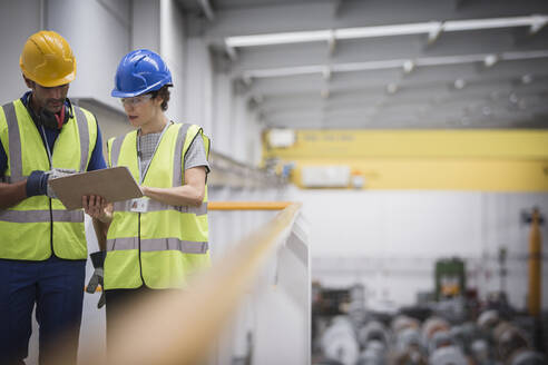 Aufsichtspersonen mit Klemmbrett im Gespräch auf einer Plattform in einer Fabrik - CAIF27076