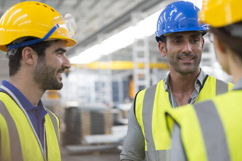 Lächelnde Arbeiter, die sich in einer Fabrik unterhalten - CAIF27077