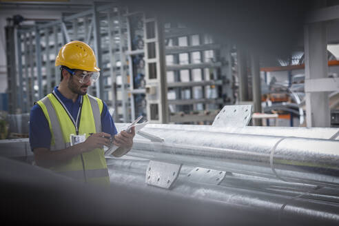 Männlicher Arbeiter mit digitalem Tablet in einem Stahlwerk - CAIF27083