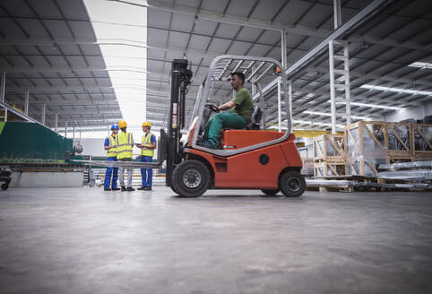 Männlicher Arbeiter fährt Gabelstapler in einer Fabrik - CAIF27097