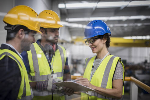 Aufsichtspersonen mit Klemmbrett im Gespräch auf einer Plattform in einer Fabrik - CAIF27105