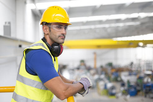 Ernste männliche Aufseher, die sich auf ein Geländer in einer Fabrik stützen - CAIF27110