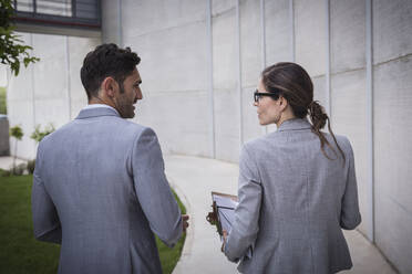 Businessman and businesswoman walking and talking on sidewalk - CAIF27117