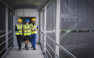 Aufsichtspersonen mit Klemmbrett, die auf einem erhöhten Gehweg vor der Fabrik gehen und sprechen - CAIF27118