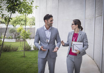 Businessman and businesswoman walking and talking on sidewalk - CAIF27124