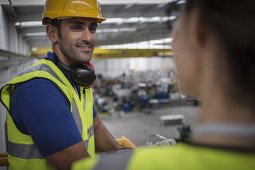 Lächelnder männlicher Vorgesetzter im Gespräch mit einem Mitarbeiter auf einer Plattform in einer Fabrik - CAIF27132