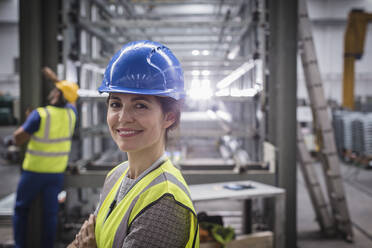 Porträt einer lächelnden, selbstbewussten Arbeiterin in einer Fabrik - CAIF27137