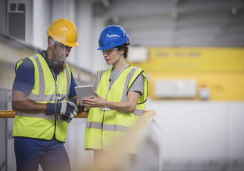 Aufsichtspersonen mit digitalem Tablet im Gespräch auf der Plattform in der Fabrik - CAIF27147