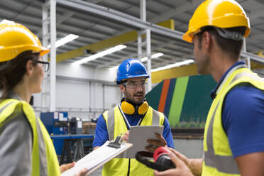 Vorgesetzter und Arbeiter mit Klemmbrett und digitalem Tablet im Gespräch in einer Fabrik - CAIF27148