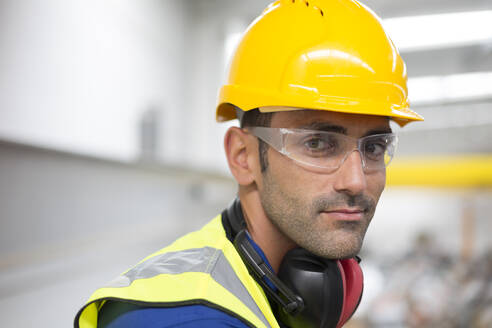 Porträt ernsthafter männlicher Arbeiter mit Schutzbrille und Schutzhelm in einer Fabrik - CAIF27150