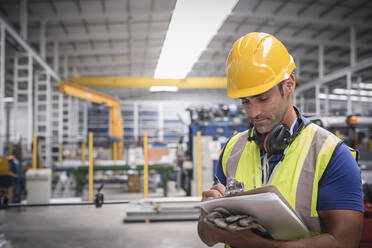 Male worker writing on clipboard in factory - CAIF27159