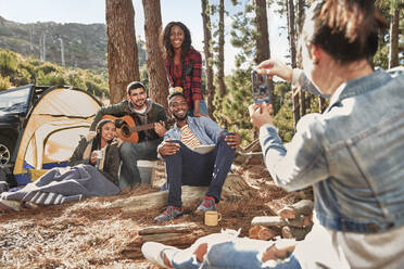 Junge Frau mit Fotohandy, die ihre Freunde auf einem Campingplatz im Wald fotografiert - CAIF27168