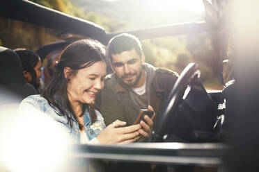 Young couple checking GPS on smart phone, enjoying road trip in jeep - CAIF27169