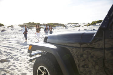 Junge Freunde laufen am sonnigen Strand in Richtung Jeep - CAIF27172
