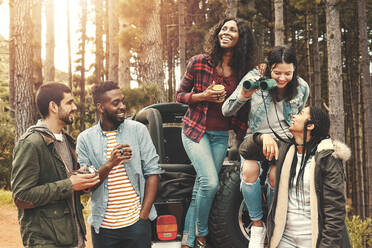 Young friends hanging out, drinking coffee at jeep in woods - CAIF27179